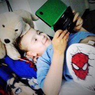 Foto: Junge mit Stoma liegt im Bett und spielt auf der Spielekonsole